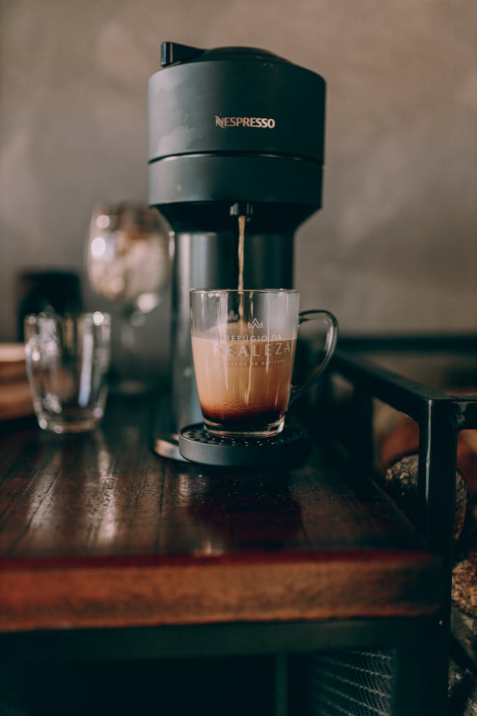 A modern coffee machine dispensing espresso into a glass mug on a wooden table, captured indoors.